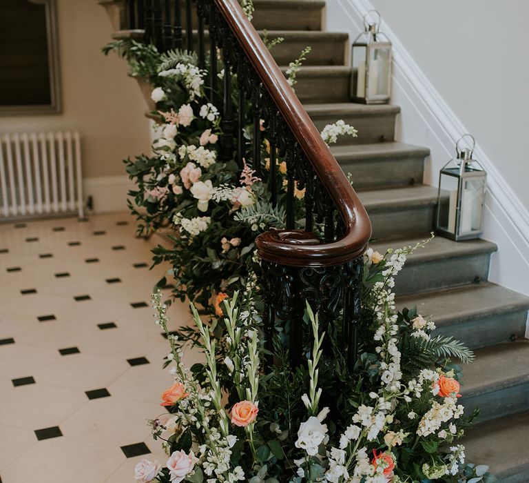 Pink, white and orange wedding flower display with silver lanterns filled with candles on stairs 