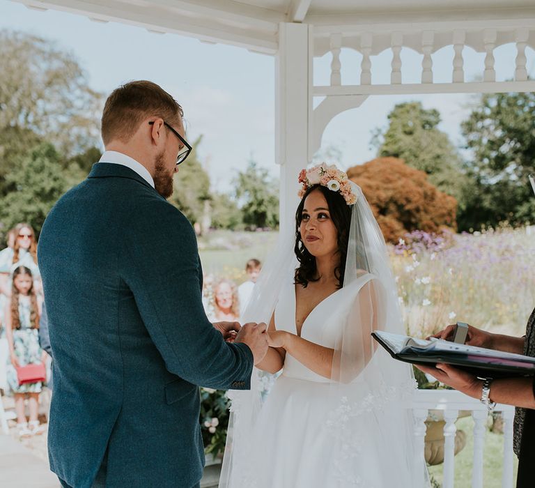 Groom in blue suit holds the bride's hands wearing Stella York wedding dress and Pronovias floral embroidery veil at outdoor ceremony