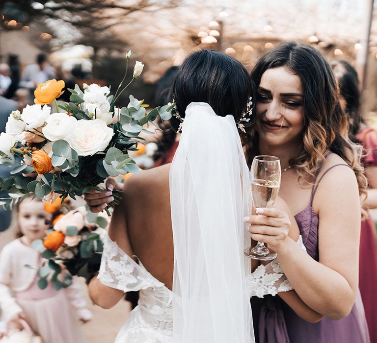 Bride carrying autumnal wedding bouquet hugs wedding guest