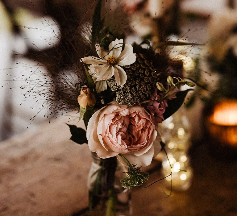 Pink rose and white cosmos with other flowers make up small flower arrangement for table setting