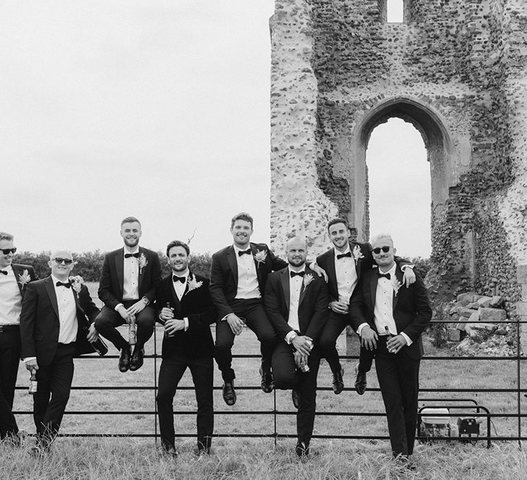 Groomsmen stand together in black tie holding bottles of beer and some wearing sunglasses 