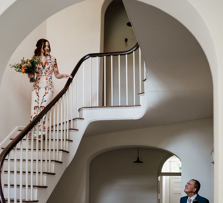 Father of the bride waits and looks up to get first look at the bride as she descends down the stairs in Temperley Bridal dress