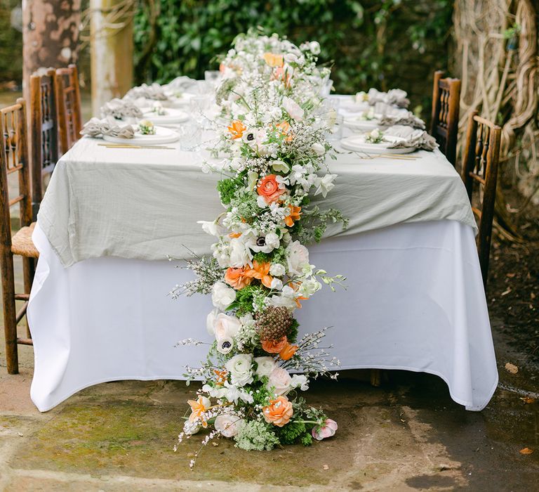 wedding flower table runner with green foliage and white and peach flowers 