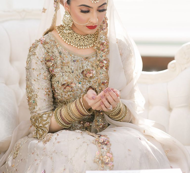 Bride cups her hands together whilst wearing traditional saree and gold bangles complete with purple nails and red lipstick 