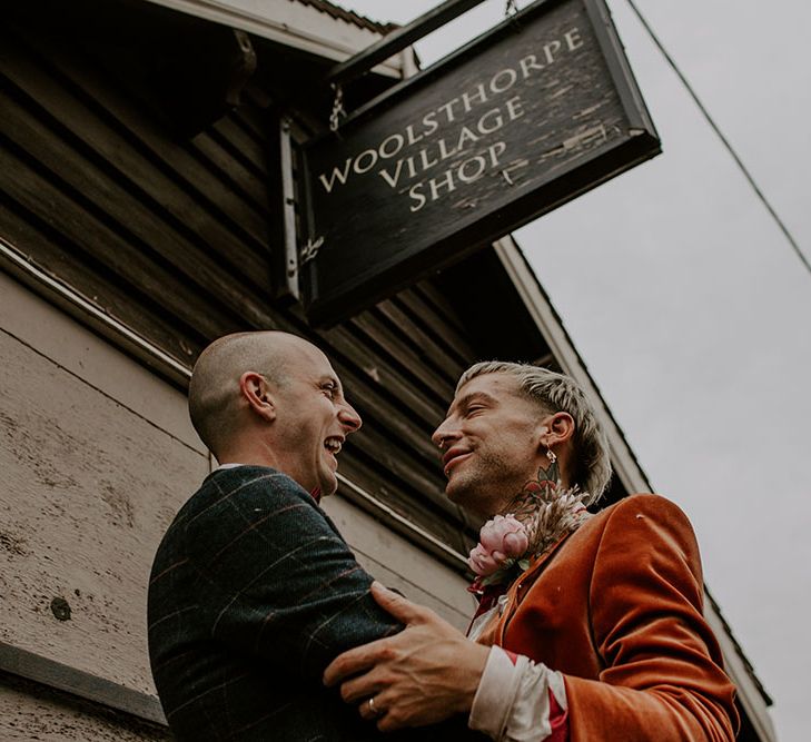 Grooms look lovingly at one another as groom wears velvet orange blazer 