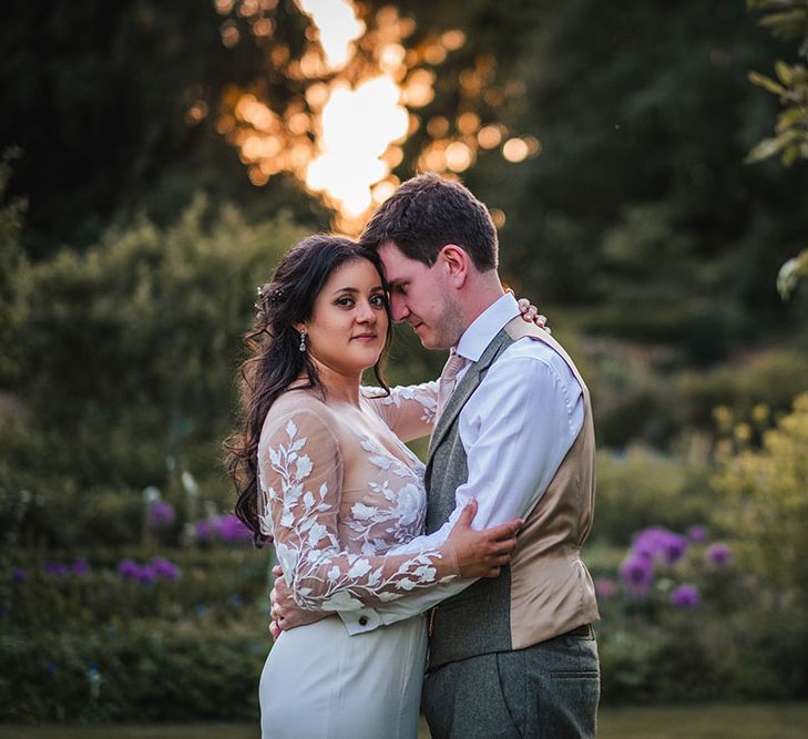 Bride wears sheer lace long sleeve embellished wedding dress as she embraces her groom outdoors on her wedding day