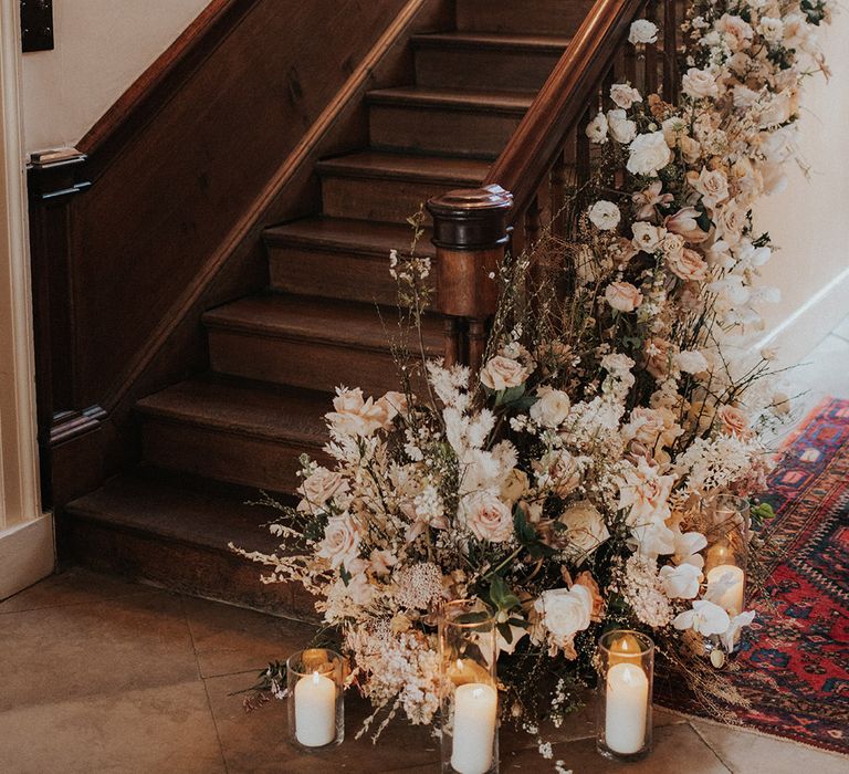 White pillar candles in hurricane vases and pink and white flowers decorate the staircase