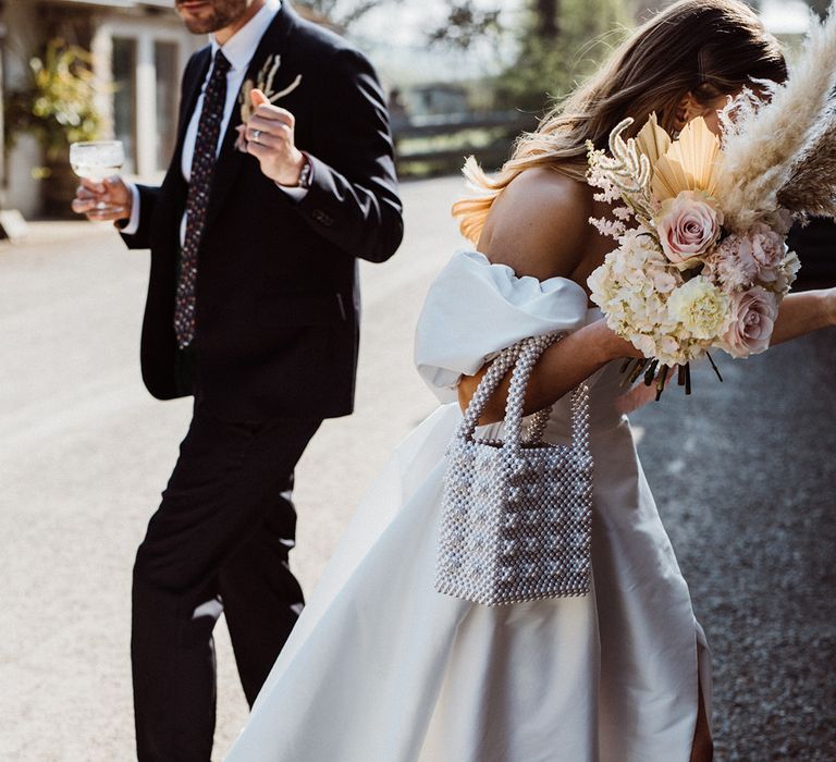 Bride with pink roses and white hydrangea wedding bouquet with dried flowers and a pearl handbag in a puff sleeve wedding dress 