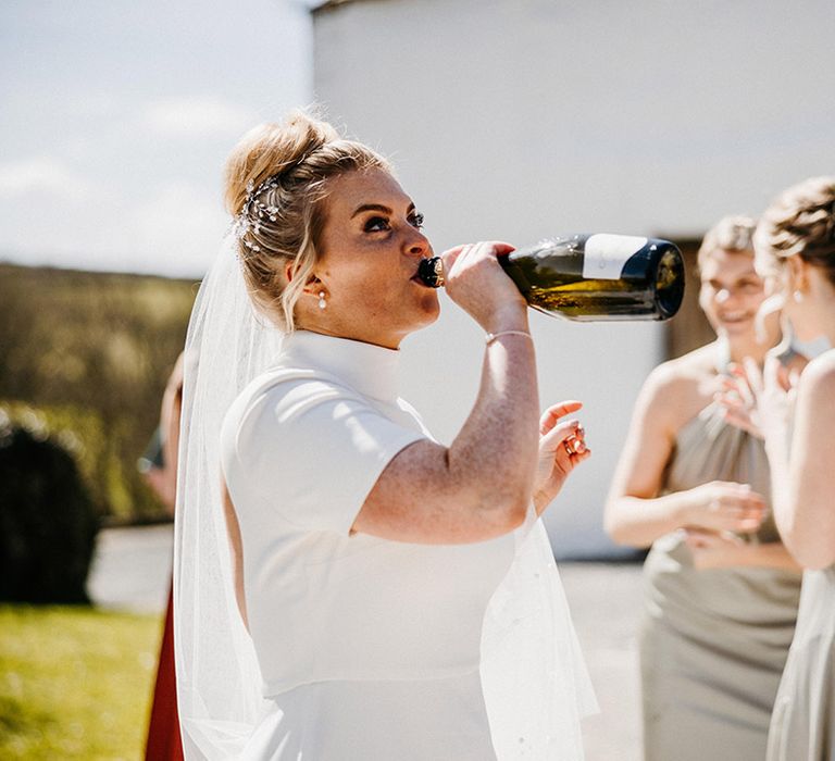 Bride in high neck Jesus Peiro wedding dress drinking from a bottle with jewelled hair accessory