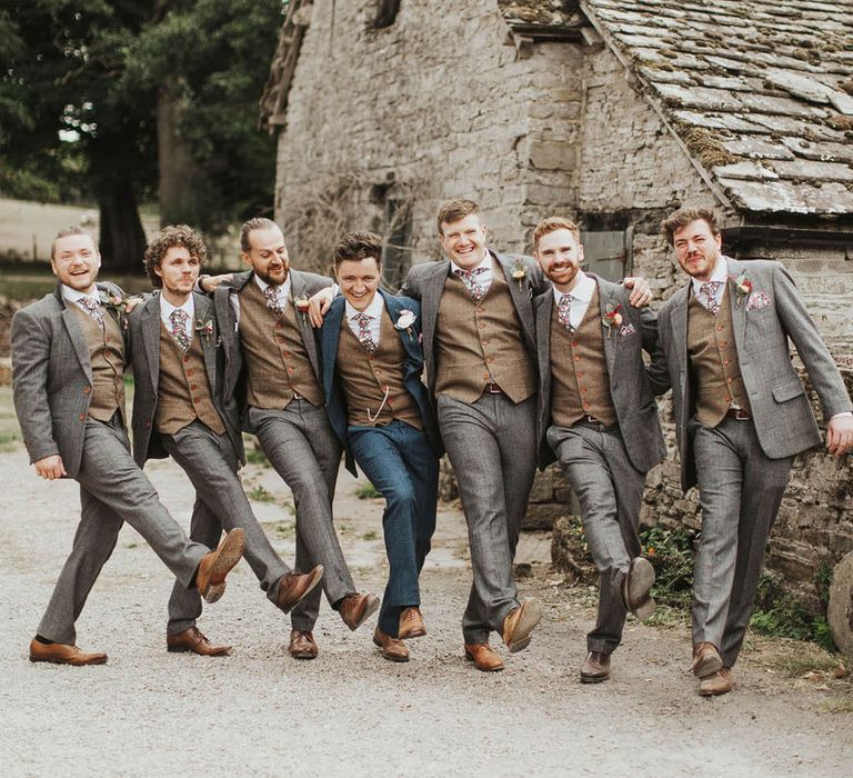 Groom in a blue suit takes a funny walking shot with the groomsmen in grey suits 