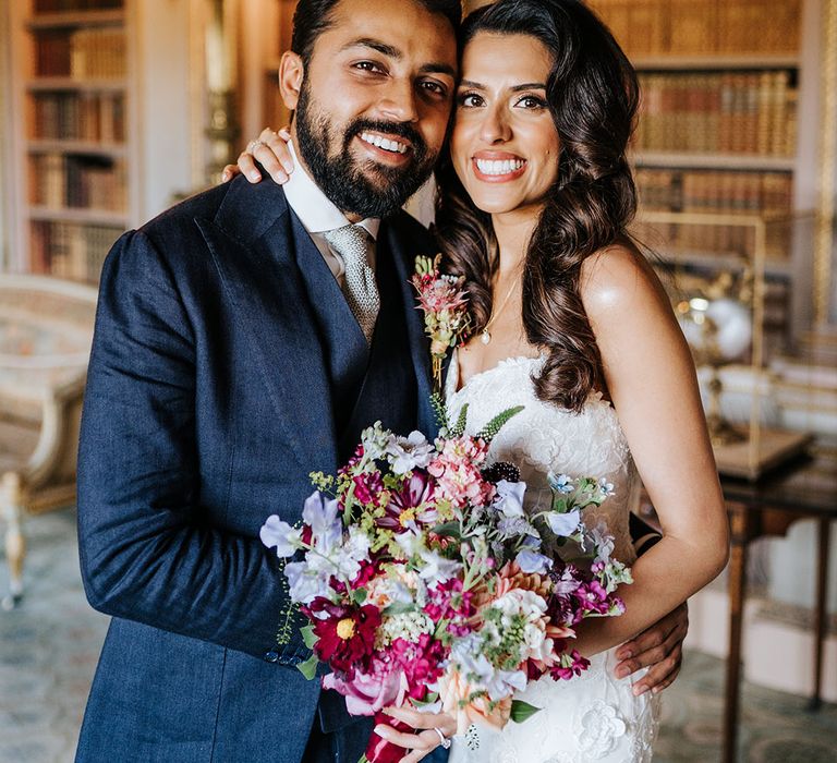 Bride holds brightly coloured floral bouquet and stands beside her groom who wears matching buttonhole 