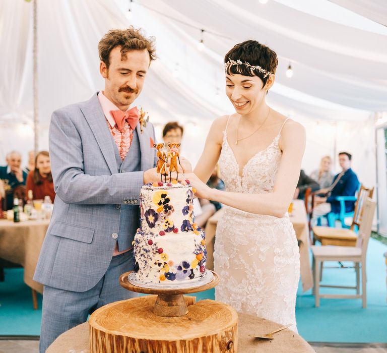 Bride & groom cut rustic wedding cake on wooden slab in secondhand marquee for back garden wedding