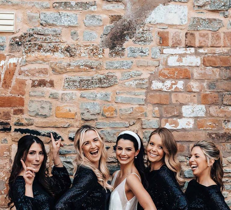 Bridesmaids wear short sparkly black bridesmaid dresses with long sleeves in front of brick wall 