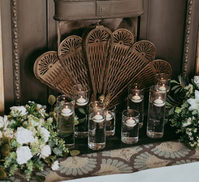 Fireplace at the hotel wedding venue decorated with white faux wedding flowers and vases filled with water and floating tea lights 