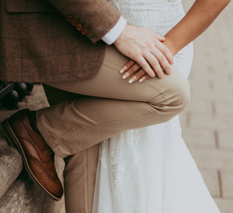 Groom in beige trousers and a checkered brown suit jacket with the bride in a glitzy wedding dress with natural rounded wedding nails 