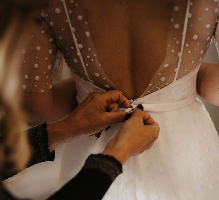 Wedding guest helps fasten the bride into her dotted wedding dress from Love Spell