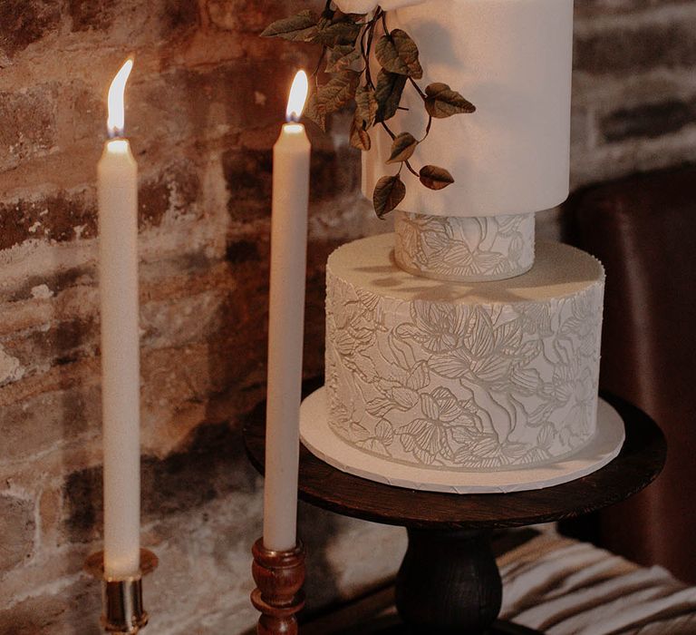 White iced and textured winter wedding cake with white rose decor and some white taper candles 