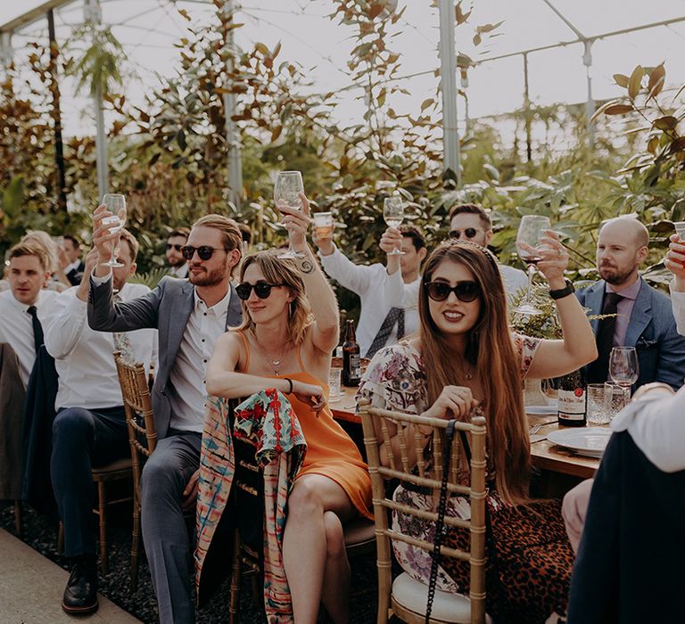 Seated guests in sunglasses raising their glasses to the Bride and Groom