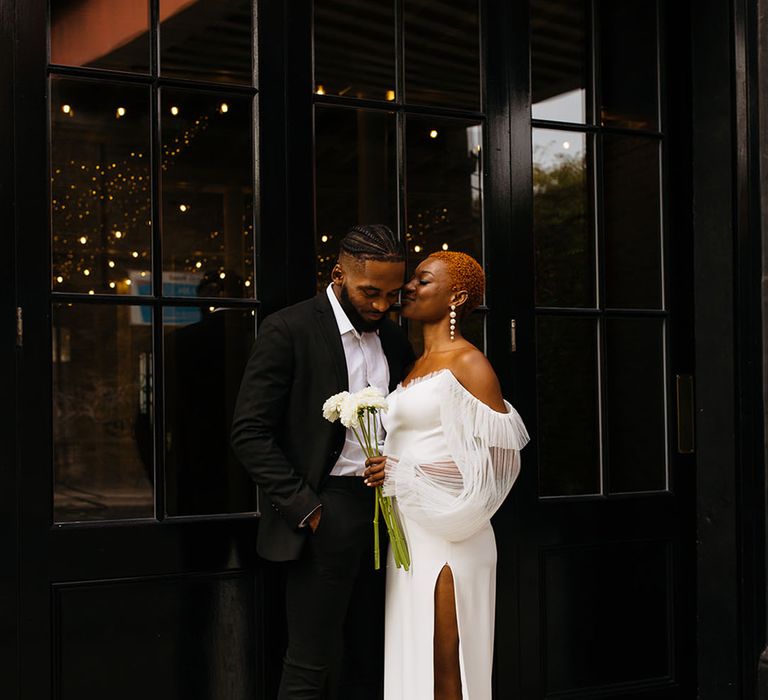 Groom in skinny black Topman tuxedo standing close to bride in off shoulder wedding dress with front slit and dramatic lace puff sleeves at 100 Barrington