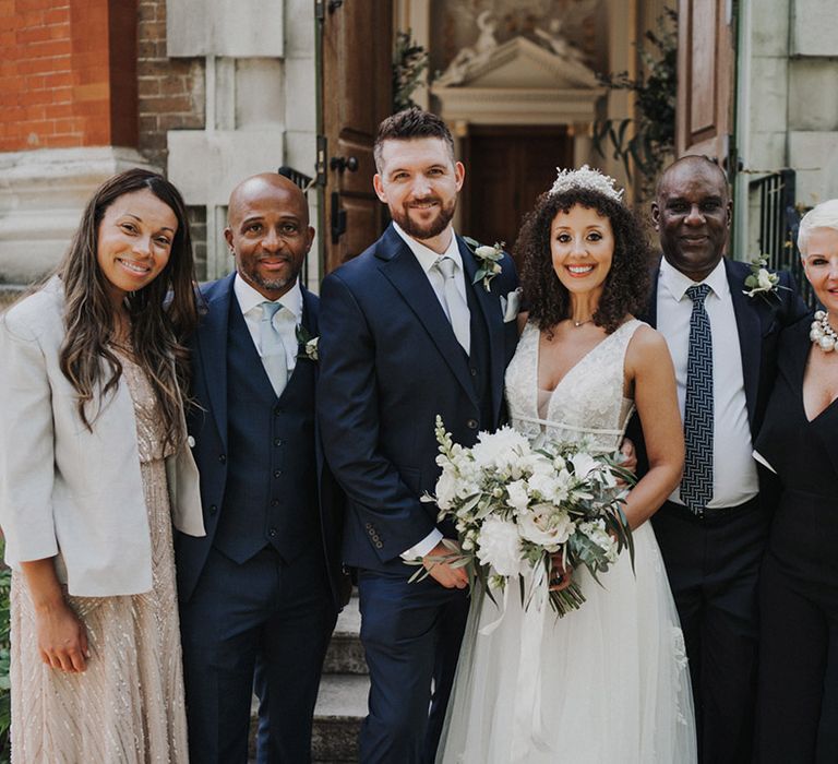 Bride holds white and green floral bouquet and stands beside groomsmen in three piece suits 