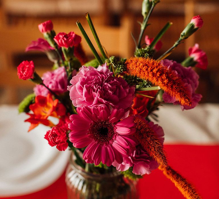 Small pink and orange floral arrangement lining banquet tables 