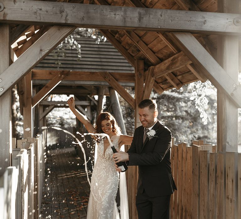 The bride and groom pop champagne at their wedding at Alnwick Treehouse wedding 