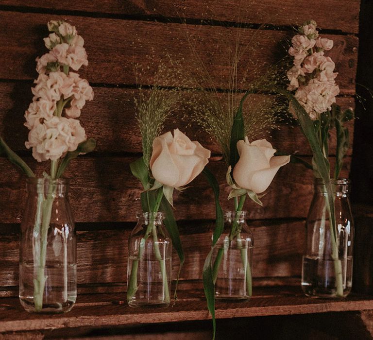 Pink delphinium and roses in small glass vases decorate the rustic Stanlake Park wedding 