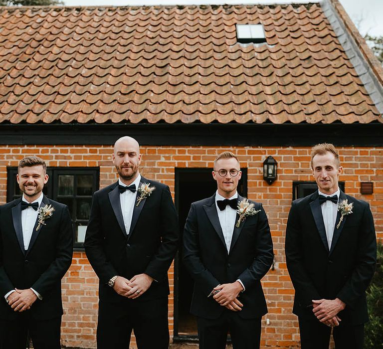 Groom and groomsmen in matching black tuxedos for the wedding with matching dried flower and bunny grass buttonholes 