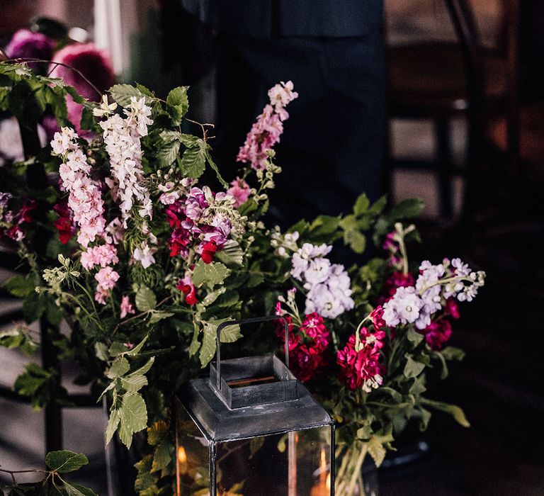 Pink and purple wildlfower arrangement with red and pink rose petals on the floor and pillar candles in glass lanterns for the romantic botanical wedding 