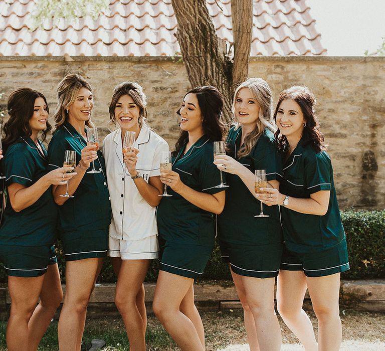 Bridesmaids in emerald green matching pyjamas with the bride in a matching white set of pyjamas with monogrammed initials