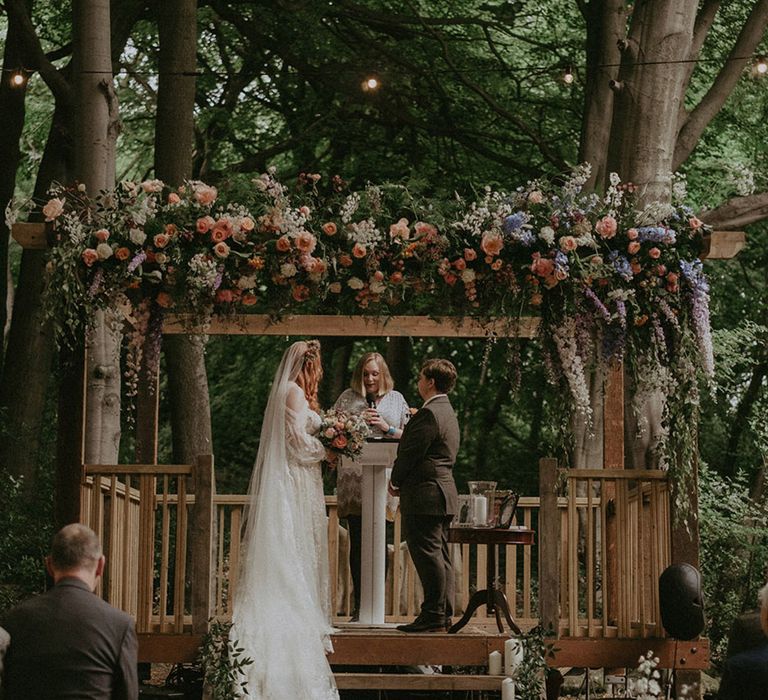 Blue, pink, and white wedding flowers decorating wooden gazebo at Lila's Wood wedding venue 