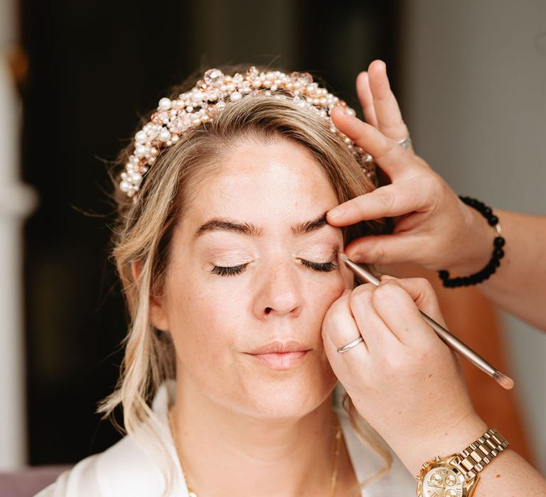 Bride wearing a pearl tiara gets her makeup done for the wedding day 