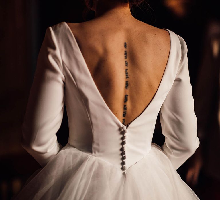 Bride wearing a long sleeve wedding dress with low back showing off her spine tattoo