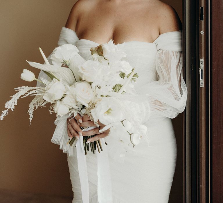 Bride in a strapless wedding dress with long sheer sleeves holding a white flower wedding bouquet 