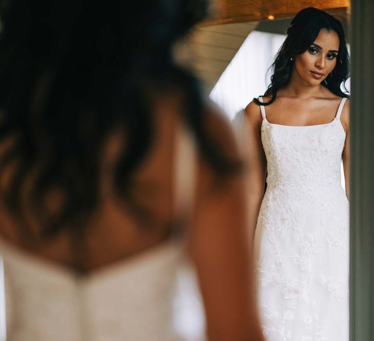 Bride in a-line tulle wedding dress with beaded lace applique with petals and a square neckline with side tulle cutouts looking in the mirror before South Farm wedding