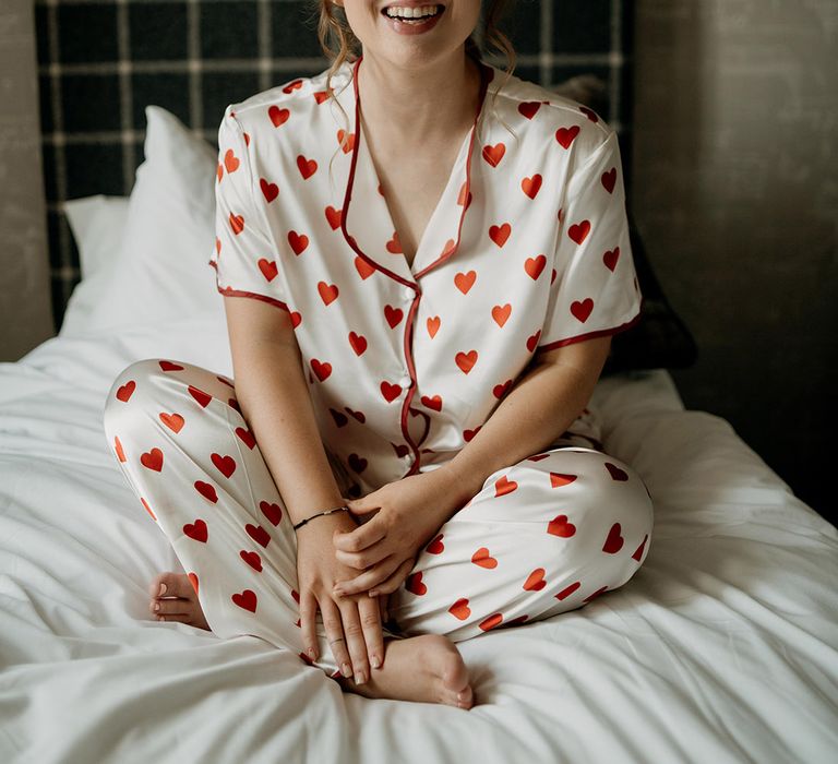 Bride in white satin pyjamas with red heart print on with matching red heart nail art design 