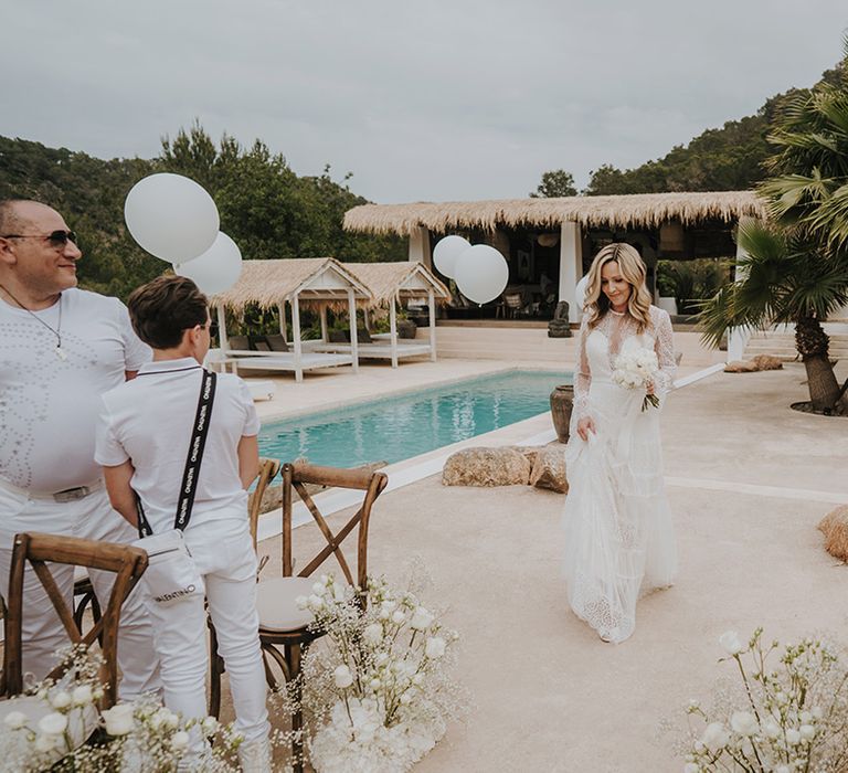 bride with long blonde wavy hair walking down the aisle in a lace wedding dress at an outdoor poolside pure house ibiza wedding ceremony