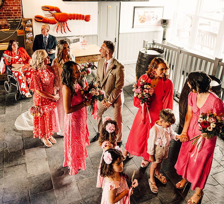 bridal party in pink and red dresses waiting to enter the wedding ceremony at East Quay wedding venue 