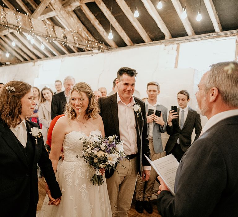 father of the bride giving away his daughter in a strapless lace wedding dress to her bride at the altar in a navy suit 