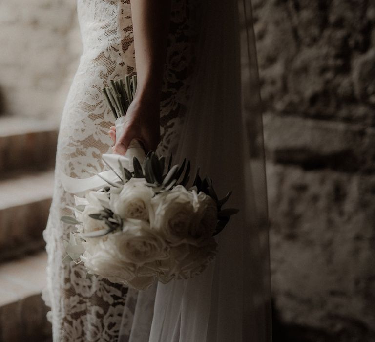 Bride in lace gown holding white rose wedding bouquet 