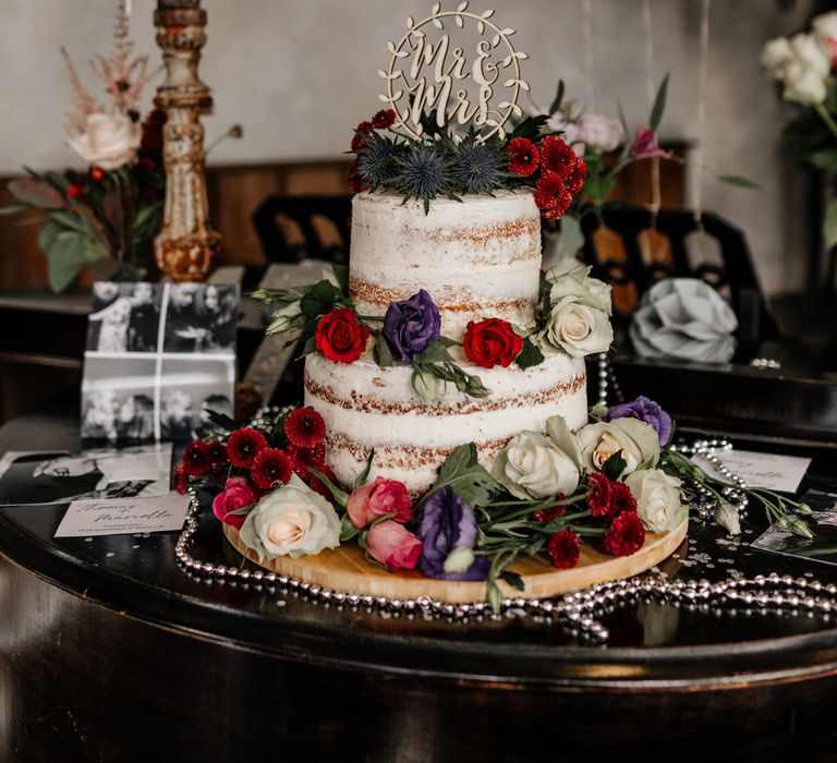 Semi naked wedding cake decorated with flowers and personalised cake topper 