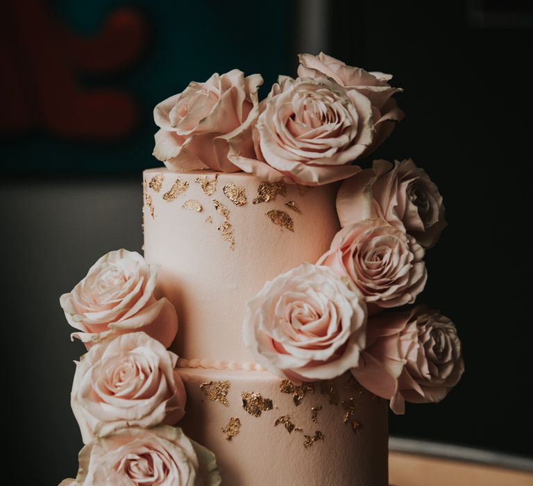 Wedding cake complete with pale pink rose decor, pink frosting and gold leaf 