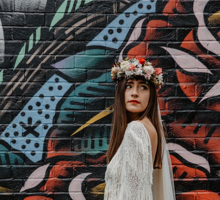 Bride in white tassel dress poses against vibrant graffiti wall