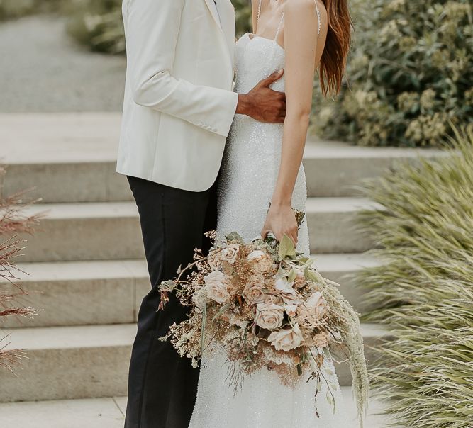 Bride with long brown hair and red lipstick wearing a sparkly wedding dress with thin straps holding a neutral bouquet 