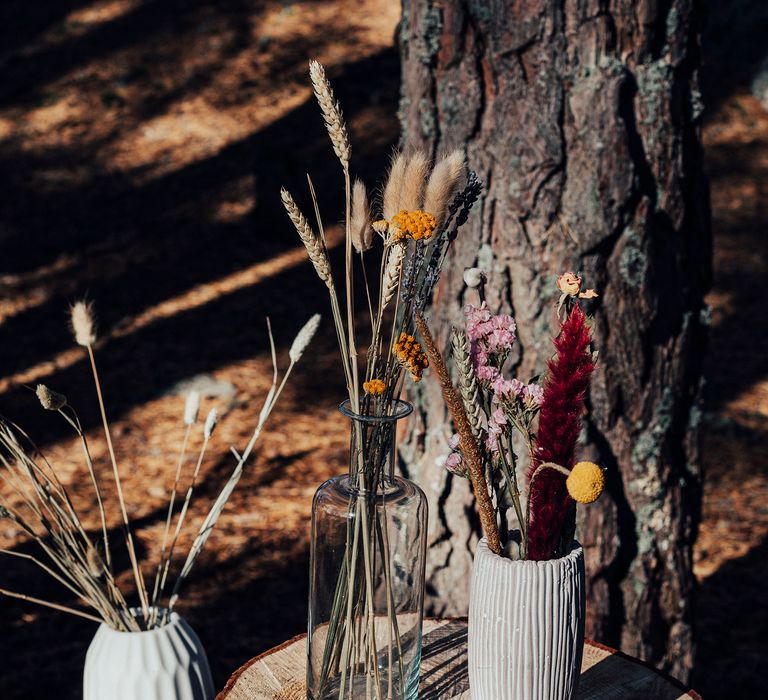 Vases with dried flowers on top of tree trunk in woodland setting