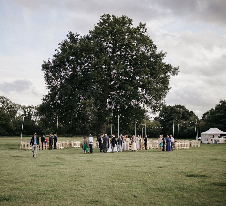 Outdoor micro wedding drinks reception with festoon light decor and picket fence 