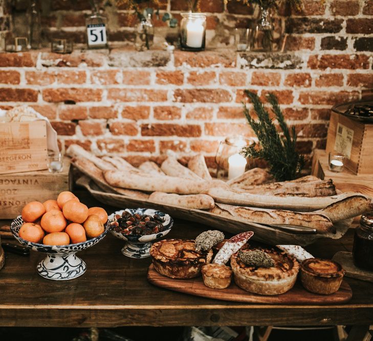 A table is set up with a selection of French breads and clementines. tHere is a cake made of cheese rounds.