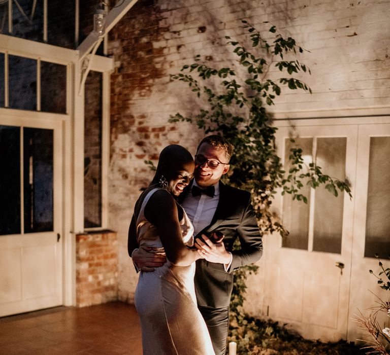 Bride with alopecia enjoying her intimate first dance on a wool rug surrounded by chandeliers 