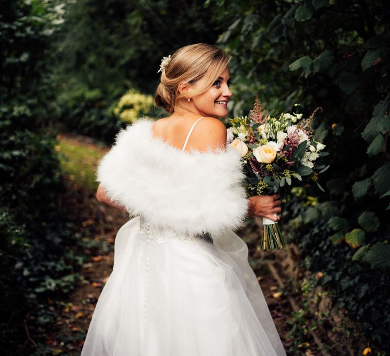 Bride wears white shawl whilst walking holding classic bouquet