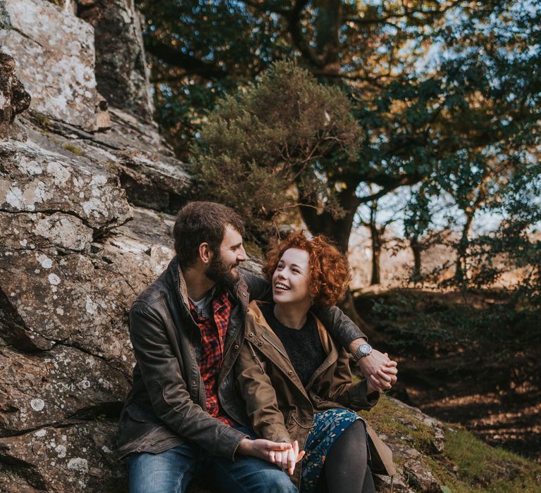 Couple sit together on a rock and laugh during pre wedding shoot